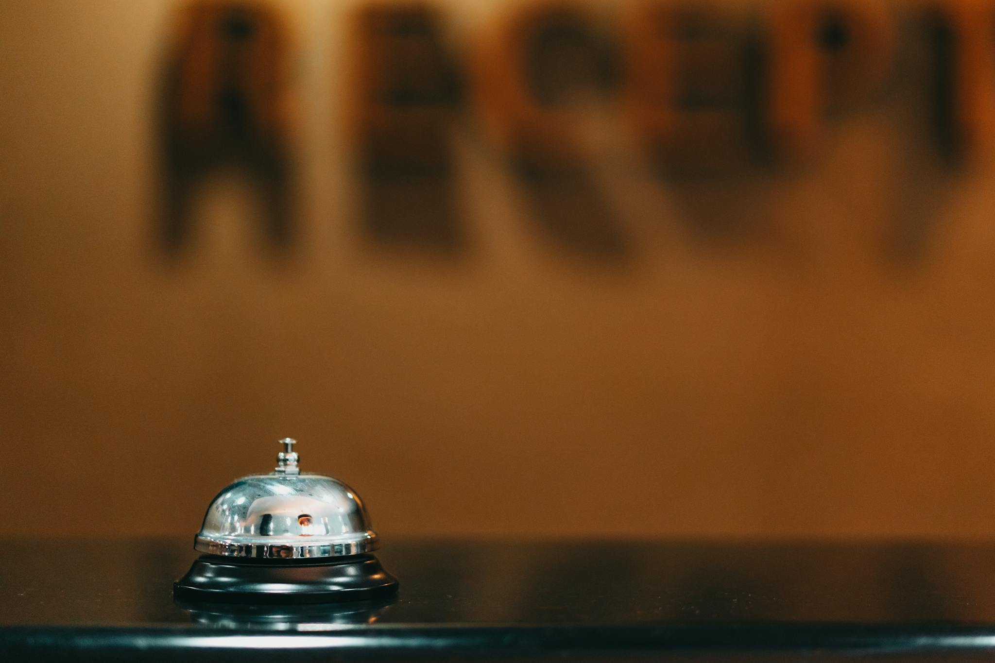 Close-up image of a silver hotel bell on a black surface with 'RECEPTION' blurred in the background.